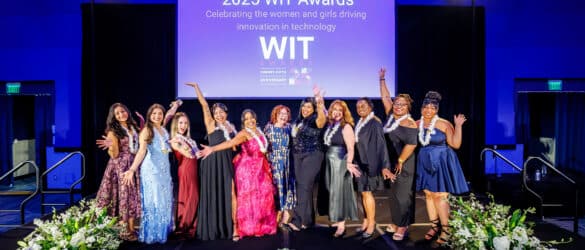 A group of women in formal attire pose on stage in front of a screen that reads 2025 WIT Awards: Celebrating the women and girls driving innovation in technology..