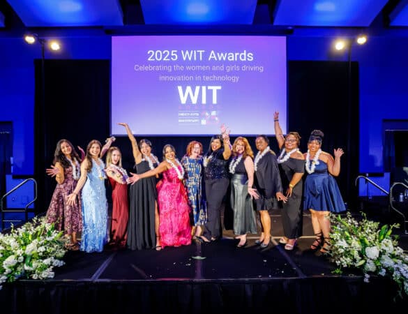 A group of women in formal attire pose on stage in front of a screen that reads 2025 WIT Awards: Celebrating the women and girls driving innovation in technology..