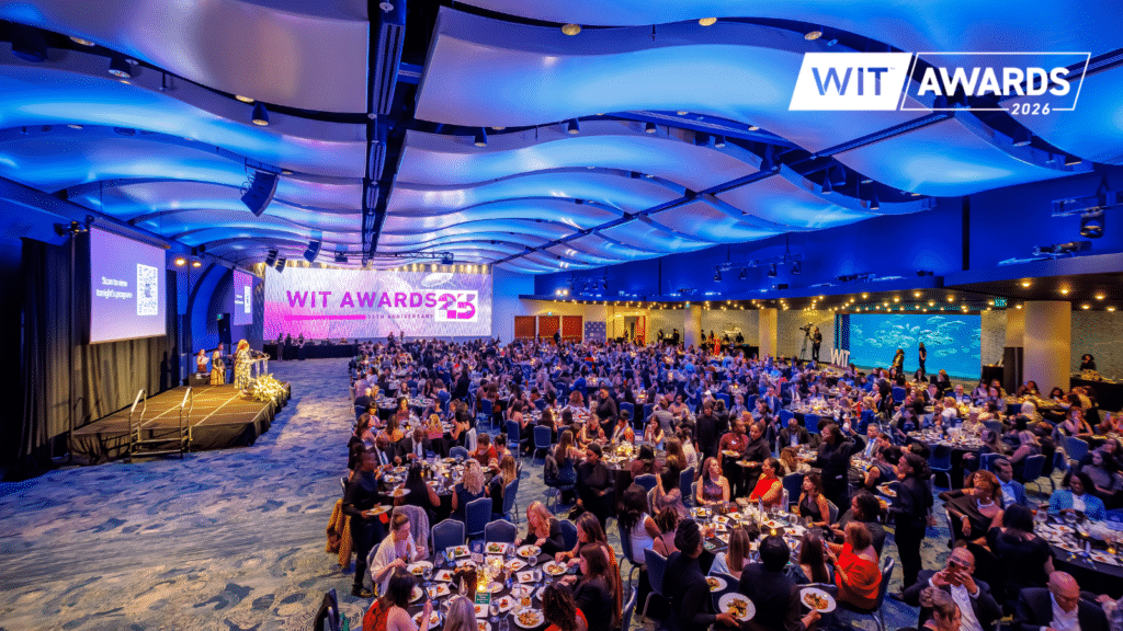 A large crowd attends the WIT Awards 2023 ceremony in a spacious, modern hall with blue lighting, decorated tables, a stage with speakers, and an aquarium visible on the right wall.